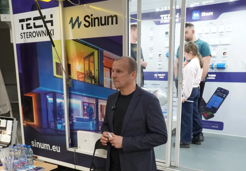 Przemysław Sobczyk, Szef Sprzedaży w Tech Sterowniki, na stoisku firmy podczas targów nieruchomości w hali Urania w Olsztynie 2025. W tle ekspozycja systemu Sinum oraz inteligentnych sterowników ogrzewania i oświetlenia.